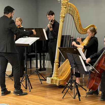Small chamber ensemble with harp, violin, and cello performing indoors with a conductor