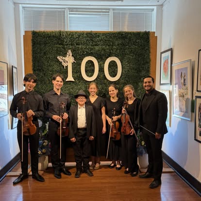 Seven musicians posing in front of a botanical "100" display in an art gallery